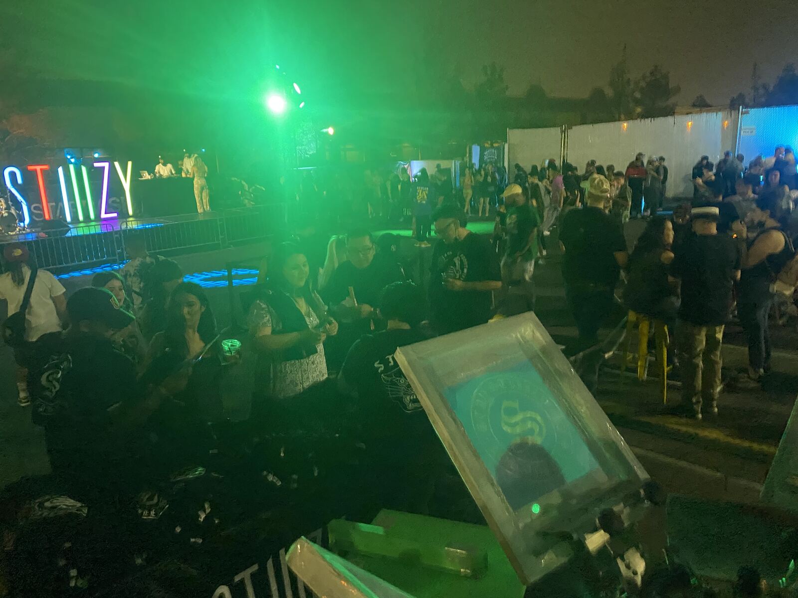 Festival event at night with neon UV signage, crowds, and vibrant green lighting